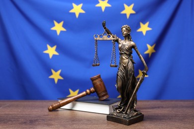 Figure of Lady Justice, judge's gavel and book on wooden table against European Union flag