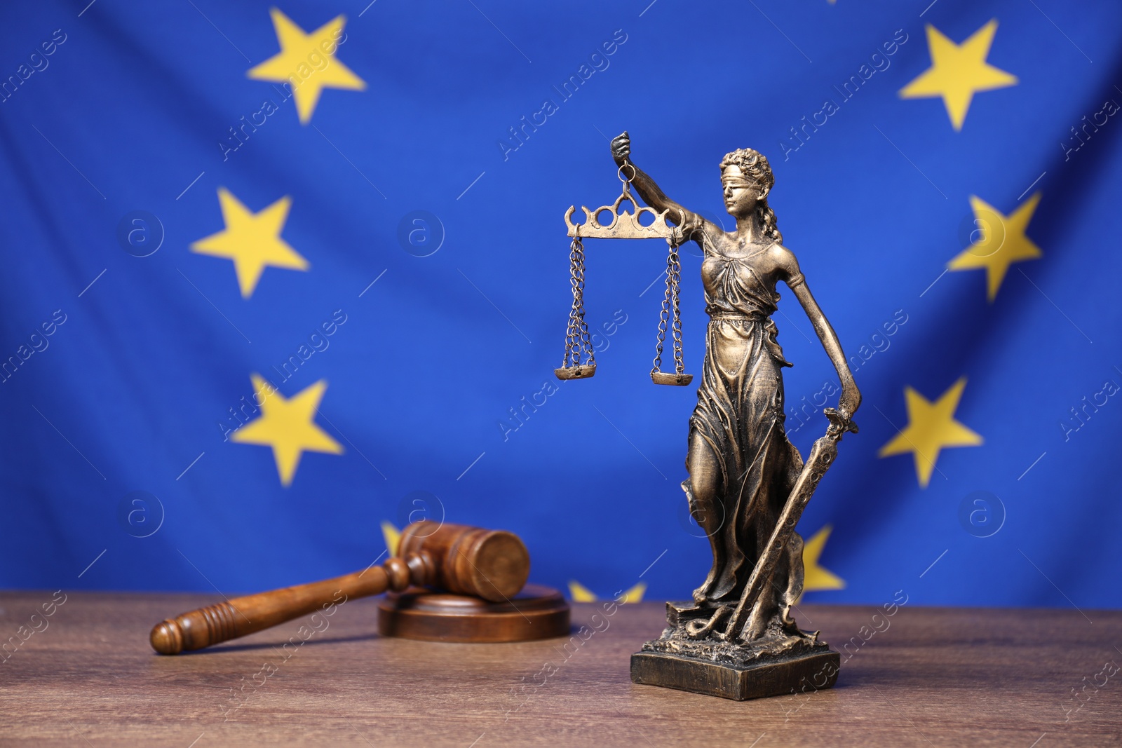 Photo of Figure of Lady Justice and judge's gavel on wooden table against European Union flag