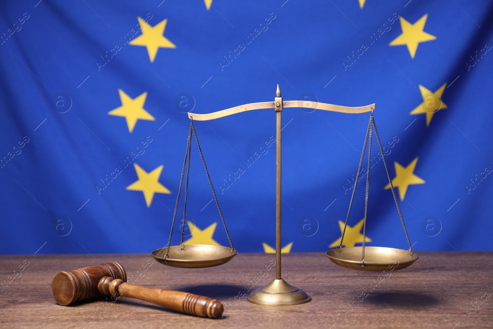 Photo of Judge's gavel and scales of justice on wooden table against European Union flag