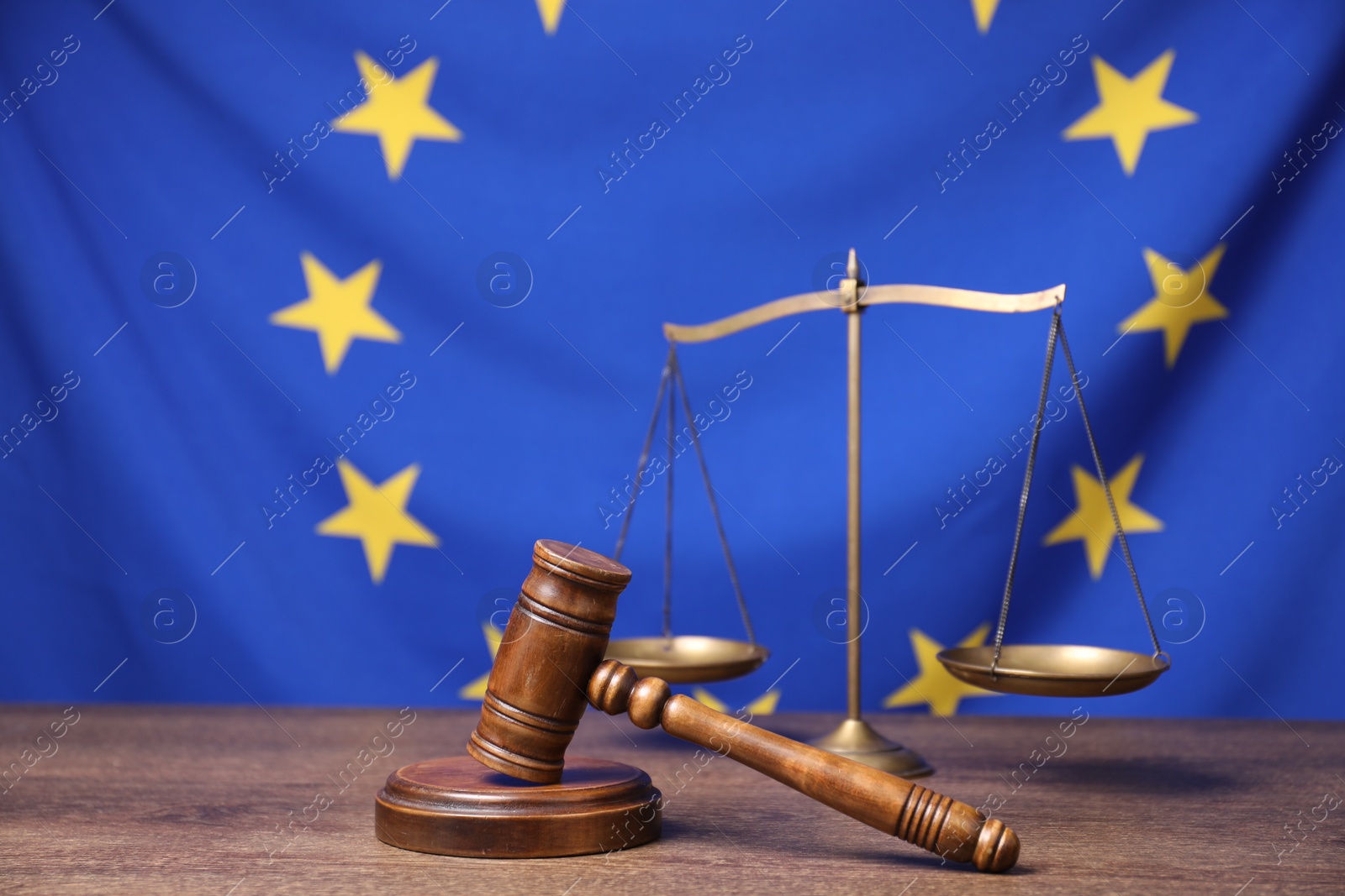 Photo of Judge's gavel and scales of justice on wooden table against European Union flag