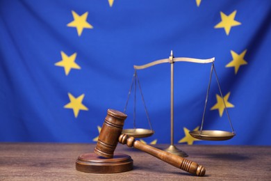 Photo of Judge's gavel and scales of justice on wooden table against European Union flag