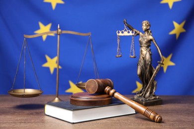 Photo of Figure of Lady Justice, judge's gavel, scales and book on wooden table against European Union flag