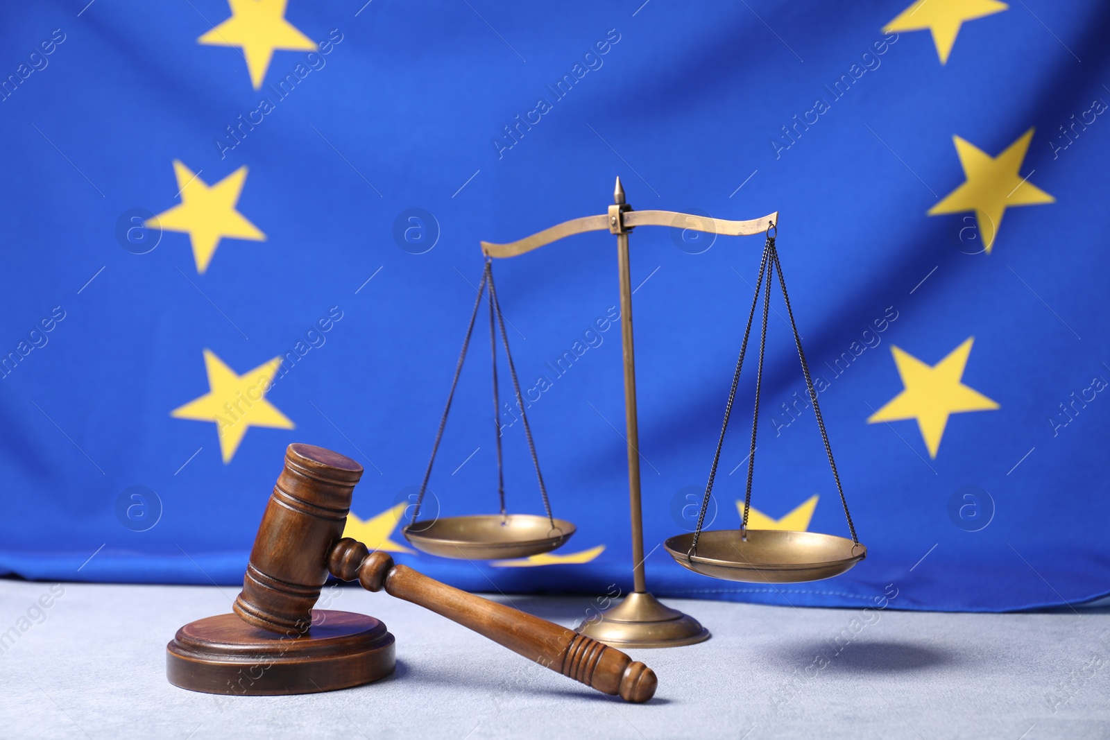 Photo of Judge's gavel and scales of justice on table against European Union flag