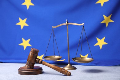 Photo of Judge's gavel and scales of justice on table against European Union flag