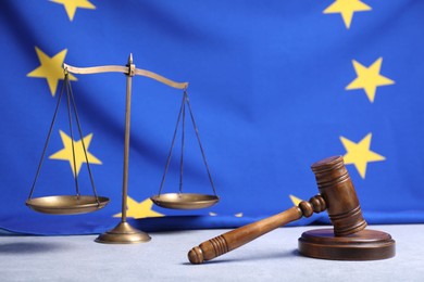 Photo of Judge's gavel and scales of justice on table against European Union flag