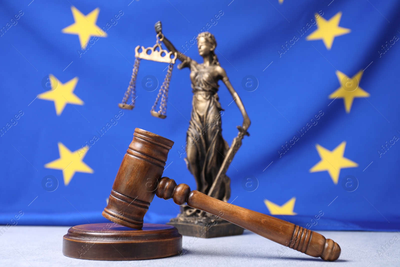 Photo of Judge's gavel and figure of Lady Justice on table against European Union flag