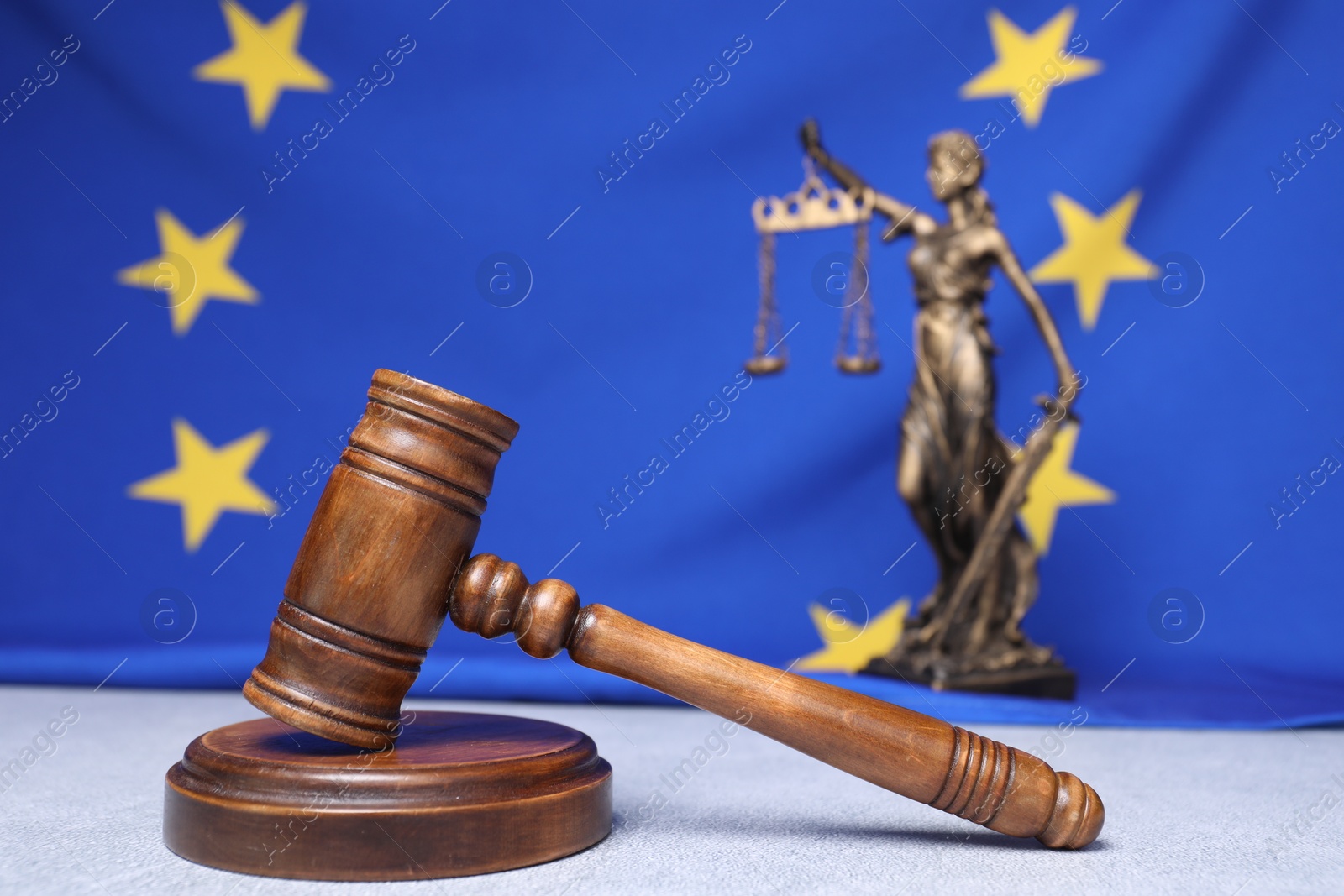 Photo of Judge's gavel and figure of Lady Justice on table against European Union flag