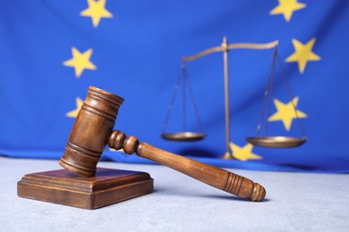 Judge's gavel and scales of justice on light grey table against European Union flag