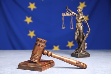 Photo of Judge's gavel and figure of Lady Justice on table against European Union flag