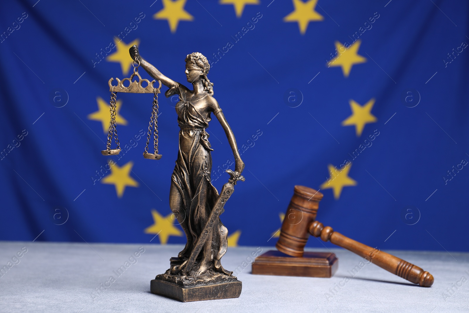 Photo of Figure of Lady Justice and judge's gavel on table against European Union flag