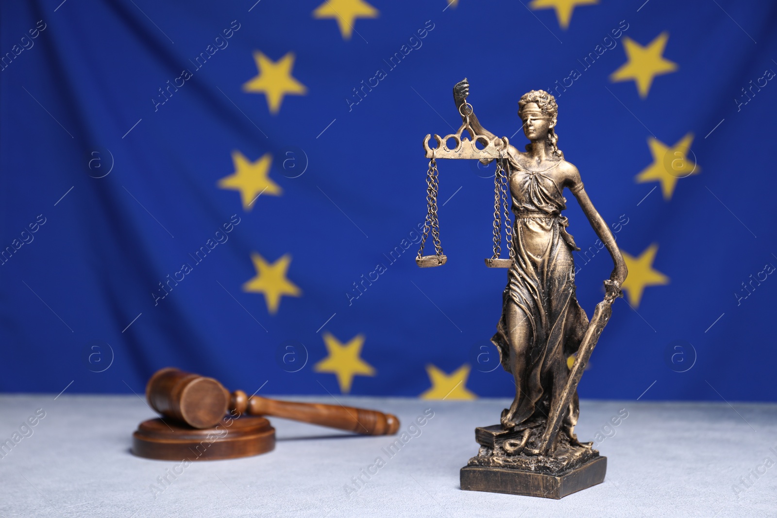 Photo of Figure of Lady Justice and judge's gavel on table against European Union flag