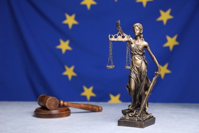 Photo of Figure of Lady Justice and judge's gavel on table against European Union flag