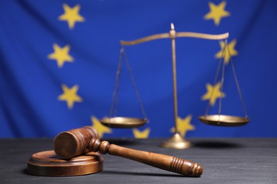 Photo of Judge's gavel and scales of justice on grey table against European Union flag