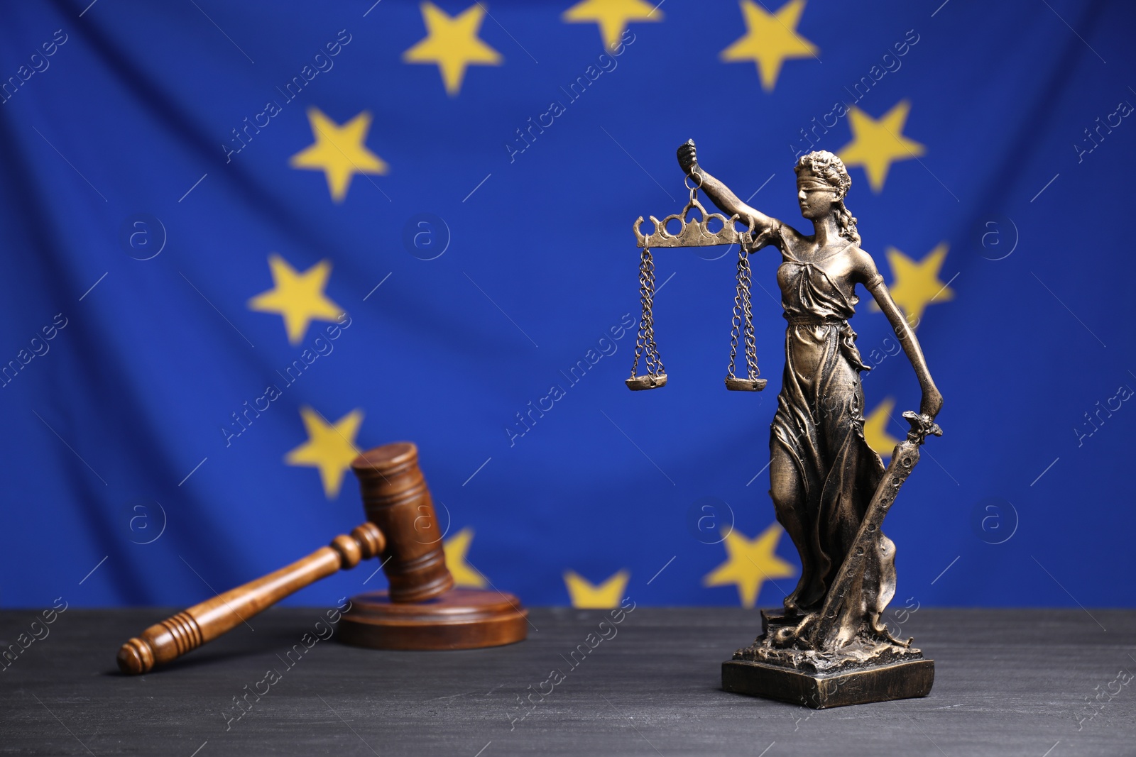 Photo of Figure of Lady Justice and judge's gavel on grey table against European Union flag