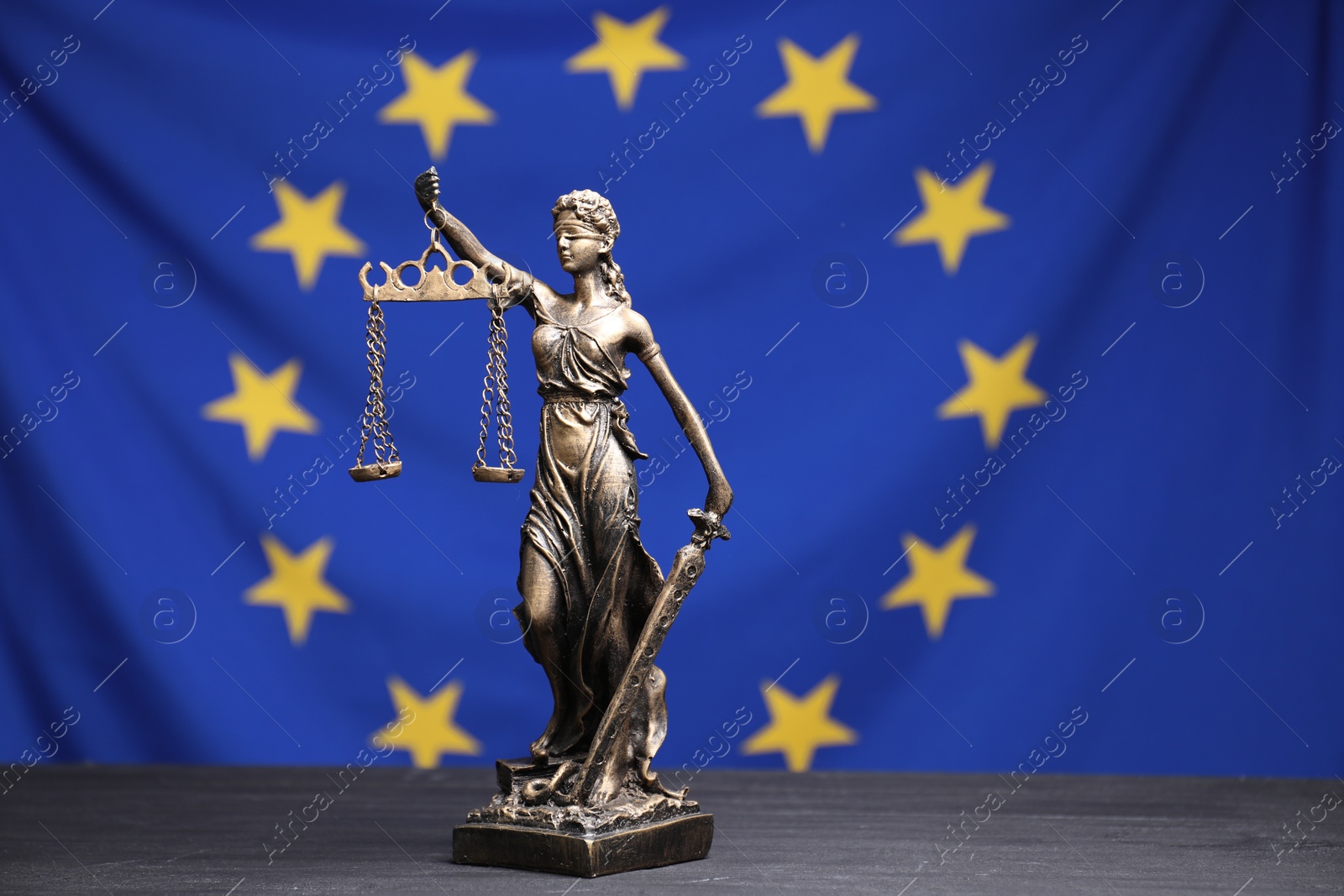 Photo of Figure of Lady Justice on grey table against European Union flag