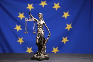 Figure of Lady Justice on grey table against European Union flag