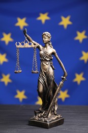 Photo of Figure of Lady Justice on grey table against European Union flag