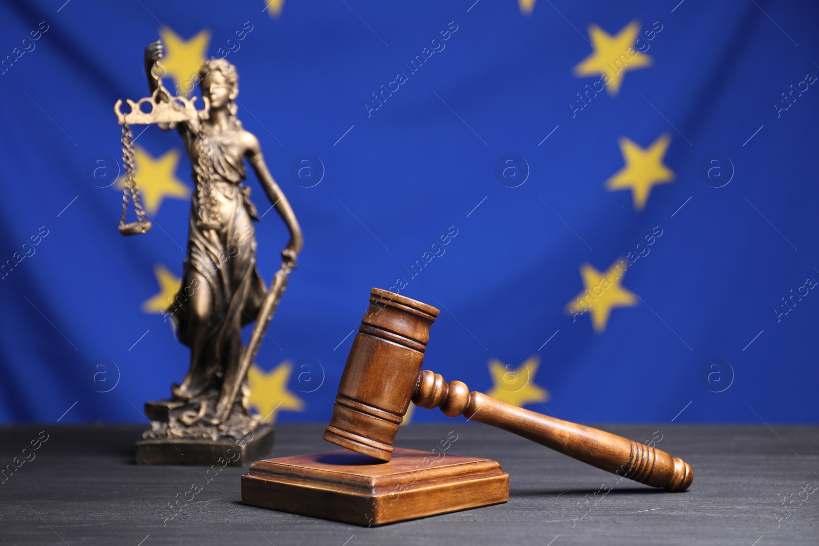 Photo of Judge's gavel and figure of Lady Justice on grey table against European Union flag