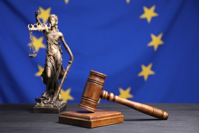 Judge's gavel and figure of Lady Justice on grey table against European Union flag