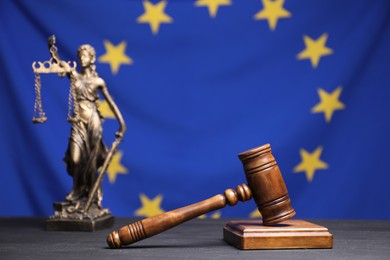 Photo of Judge's gavel and figure of Lady Justice on grey table against European Union flag