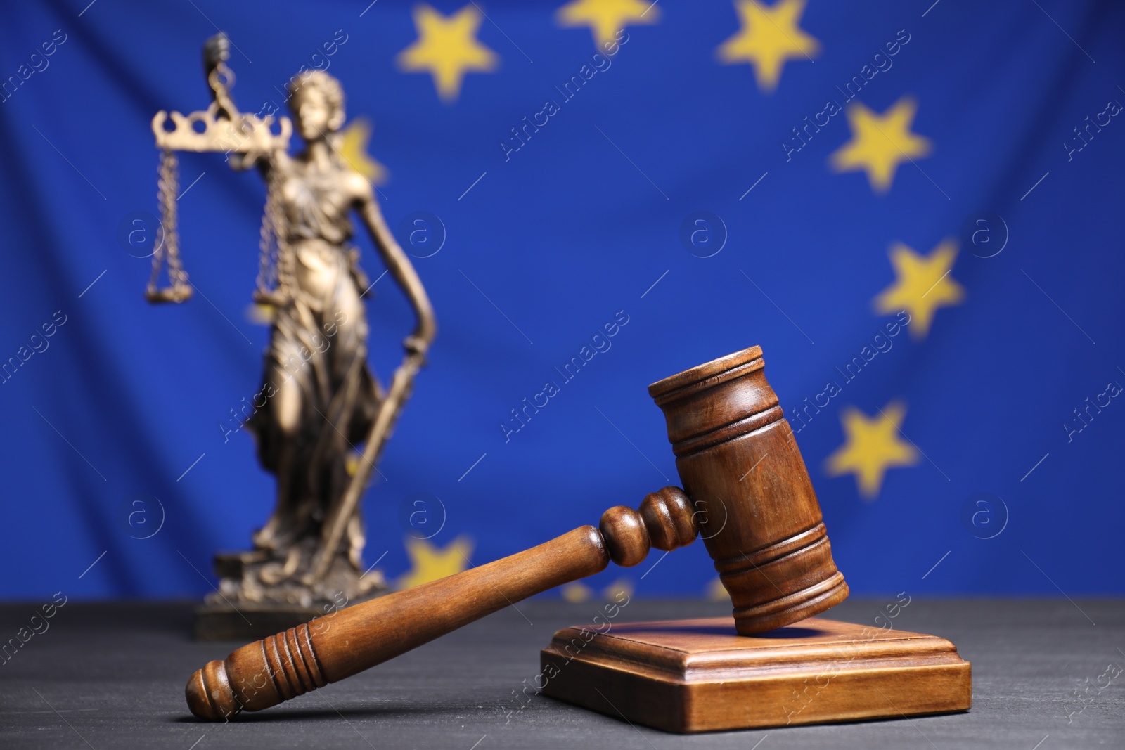 Photo of Judge's gavel and figure of Lady Justice on grey table against European Union flag