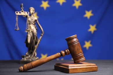 Photo of Judge's gavel and figure of Lady Justice on grey table against European Union flag