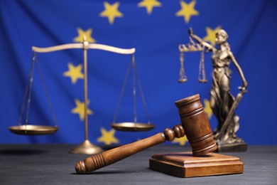 Photo of Judge's gavel, scales and figure of Lady Justice on grey table against European Union flag