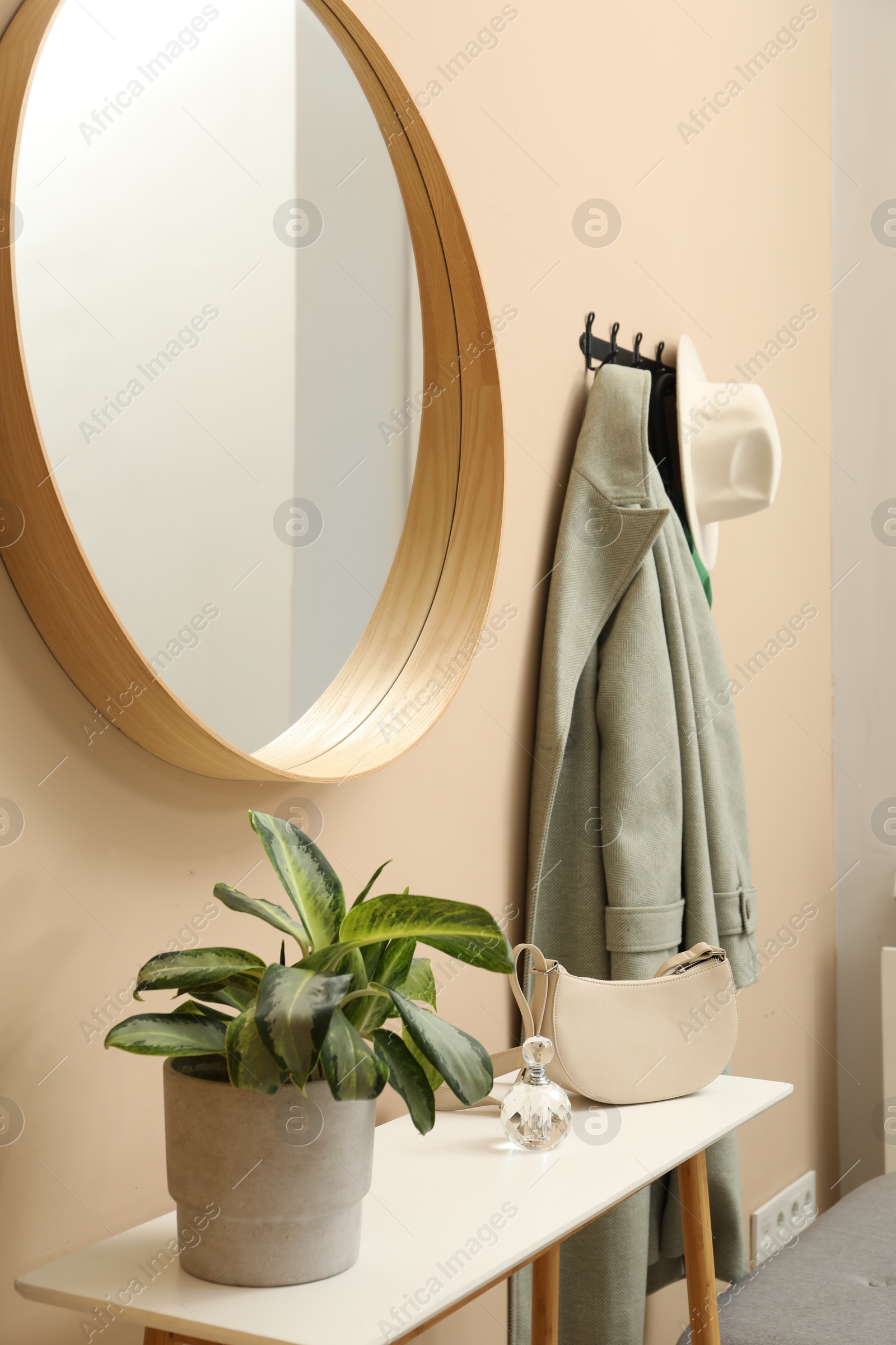 Photo of Coat rack with clothes, mirror and storage bench in hallway. Interior design