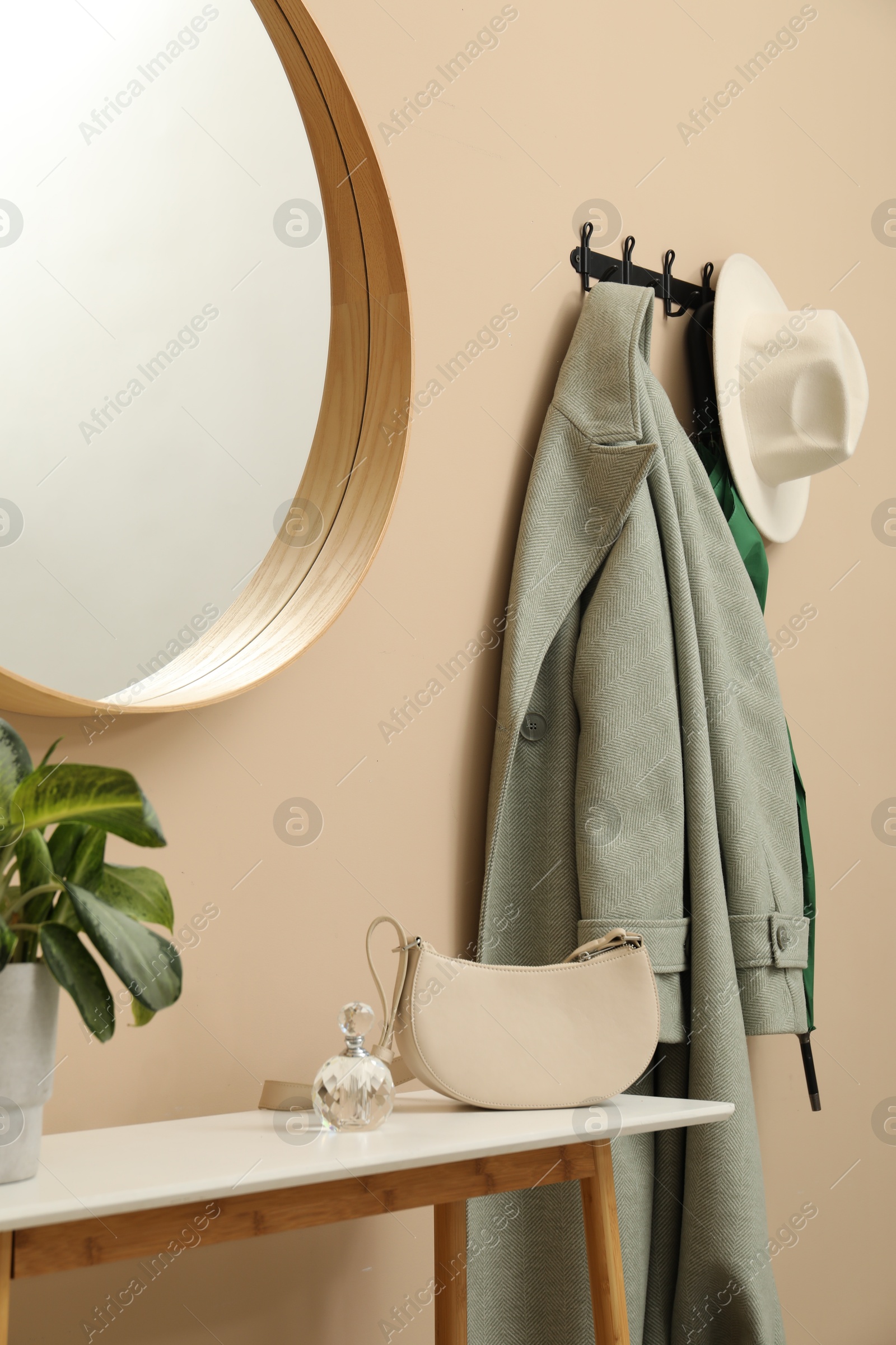 Photo of Coat rack with clothes, mirror and storage bench in hallway. Interior design