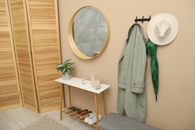 Coat rack with clothes, mirror, shoe storage benches and folding screen in hallway. Interior design