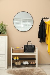 Coat rack with clothes, mirror, shoe storage bench and chest of drawers in hallway. Interior design