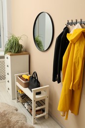 Coat rack with clothes, mirror, shoe storage bench and chest of drawers in hallway. Interior design