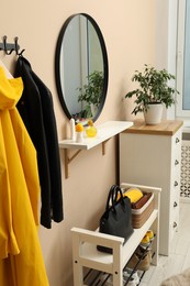 Photo of Coat rack with clothes, mirror, shoe storage bench and chest of drawers in hallway. Interior design