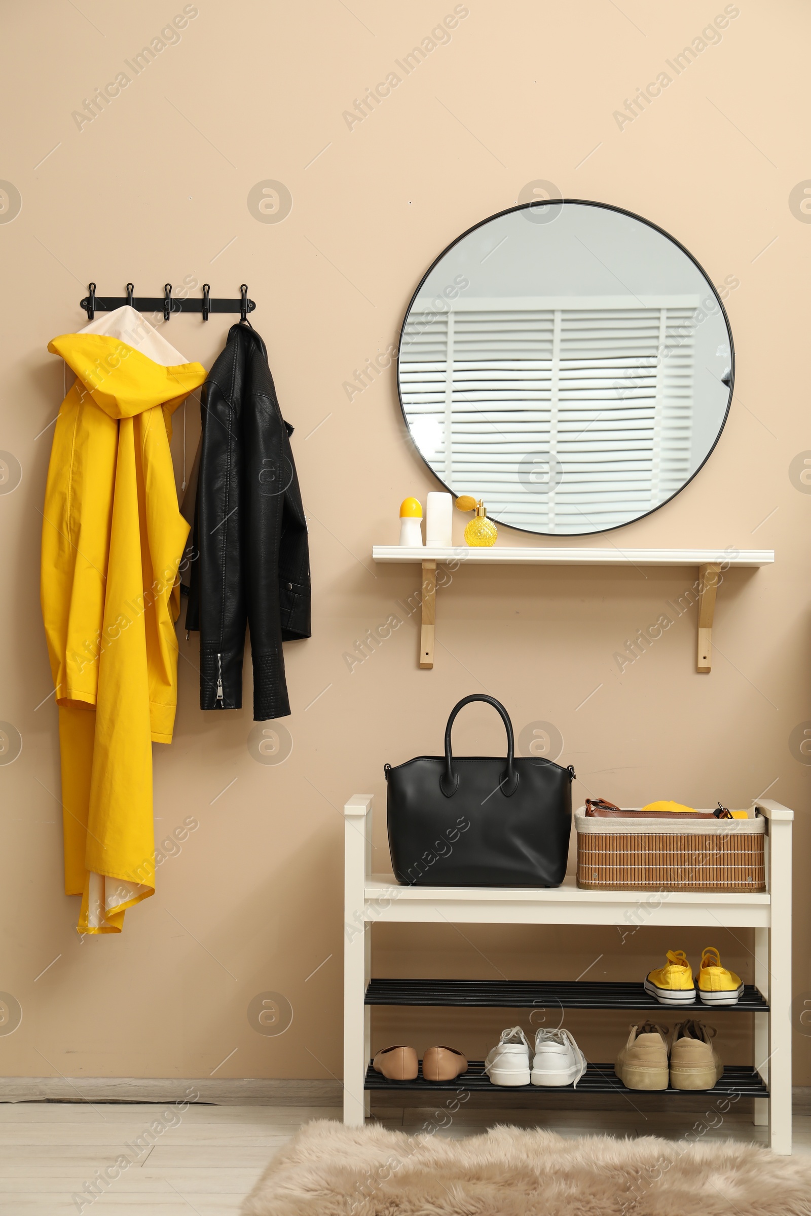 Photo of Coat rack with clothes, mirror and shoe storage bench in hallway. Interior design