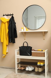 Coat rack with clothes, mirror and shoe storage bench in hallway. Interior design