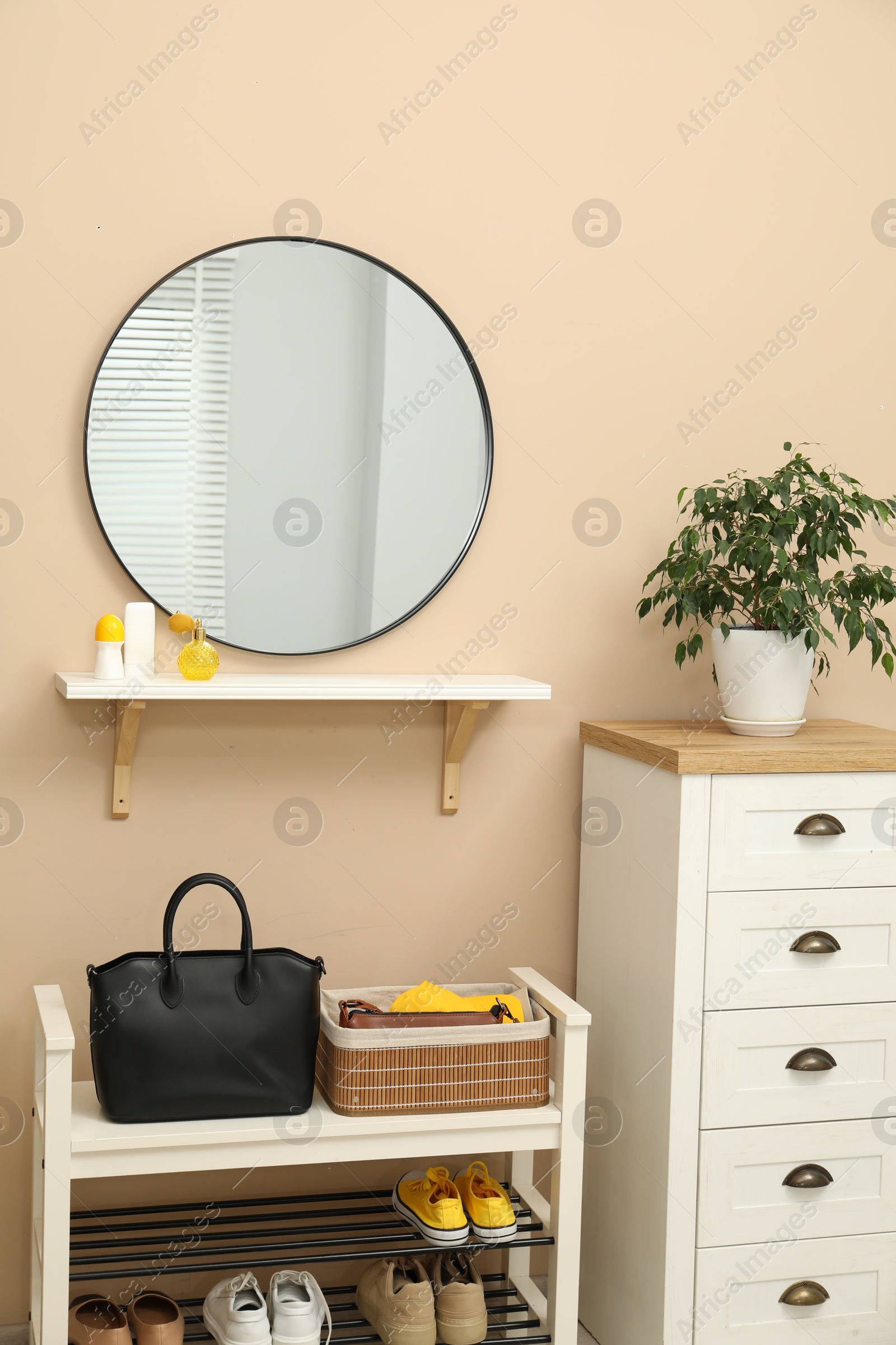 Photo of Coat rack with clothes, mirror, shoe storage bench and chest of drawers in hallway. Interior design