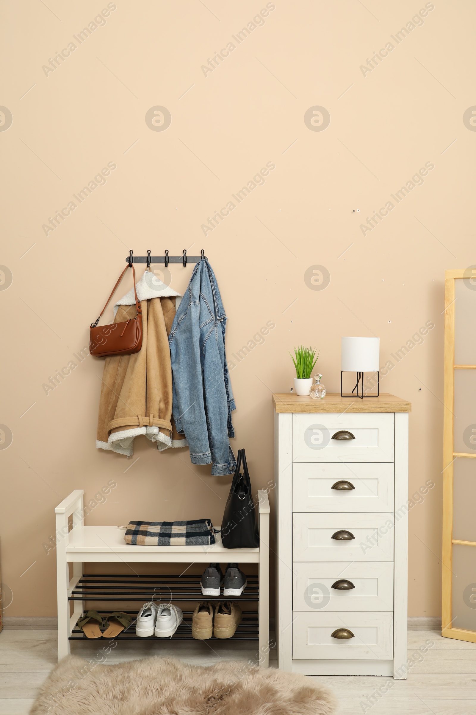 Photo of Coat rack with clothes, mirror, shoe storage bench and chest of drawers in hallway. Interior design