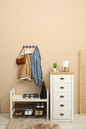 Photo of Coat rack with clothes, mirror, shoe storage bench and chest of drawers in hallway. Interior design