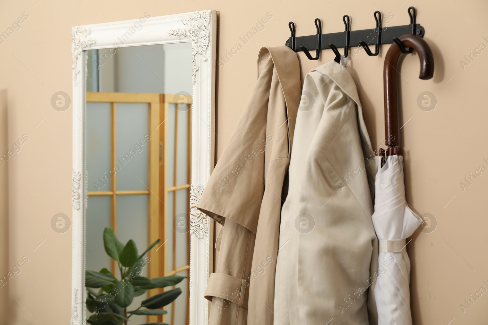 Photo of Coat rack with clothes and mirror in hallway. Interior design