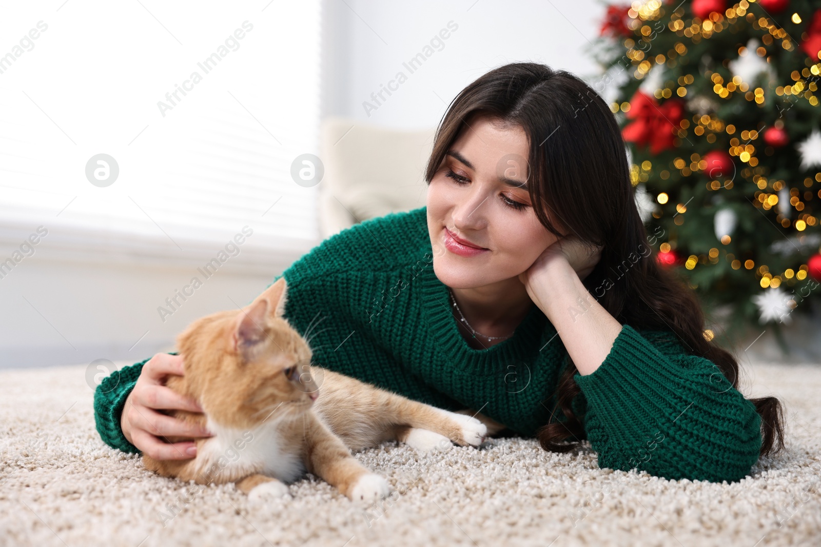 Photo of Woman with cute ginger cat lying on rug in room decorated for Christmas