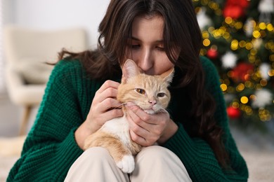 Woman kissing her cute ginger cat in room decorated for Christmas