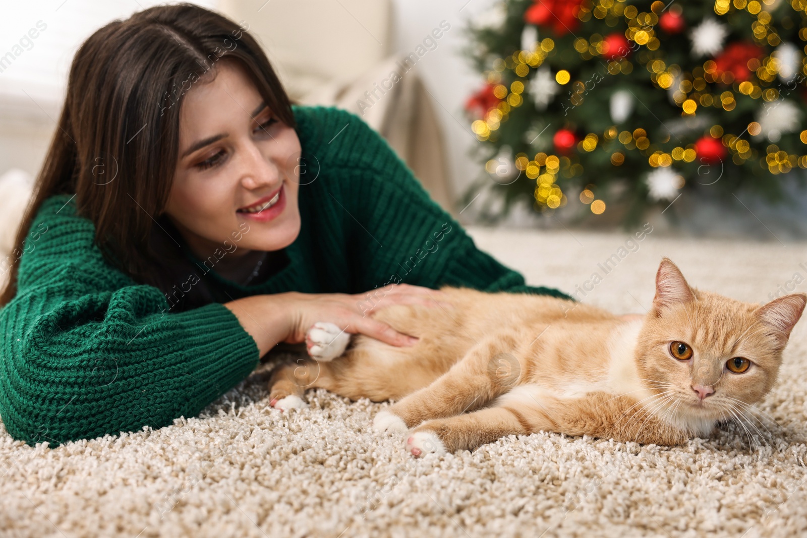 Photo of Woman with cute ginger cat lying on rug in room decorated for Christmas