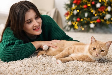 Woman with cute ginger cat lying on rug in room decorated for Christmas