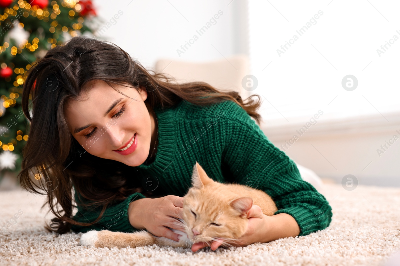 Photo of Woman with cute ginger cat lying on rug in room decorated for Christmas