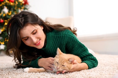 Photo of Woman with cute ginger cat lying on rug in room decorated for Christmas