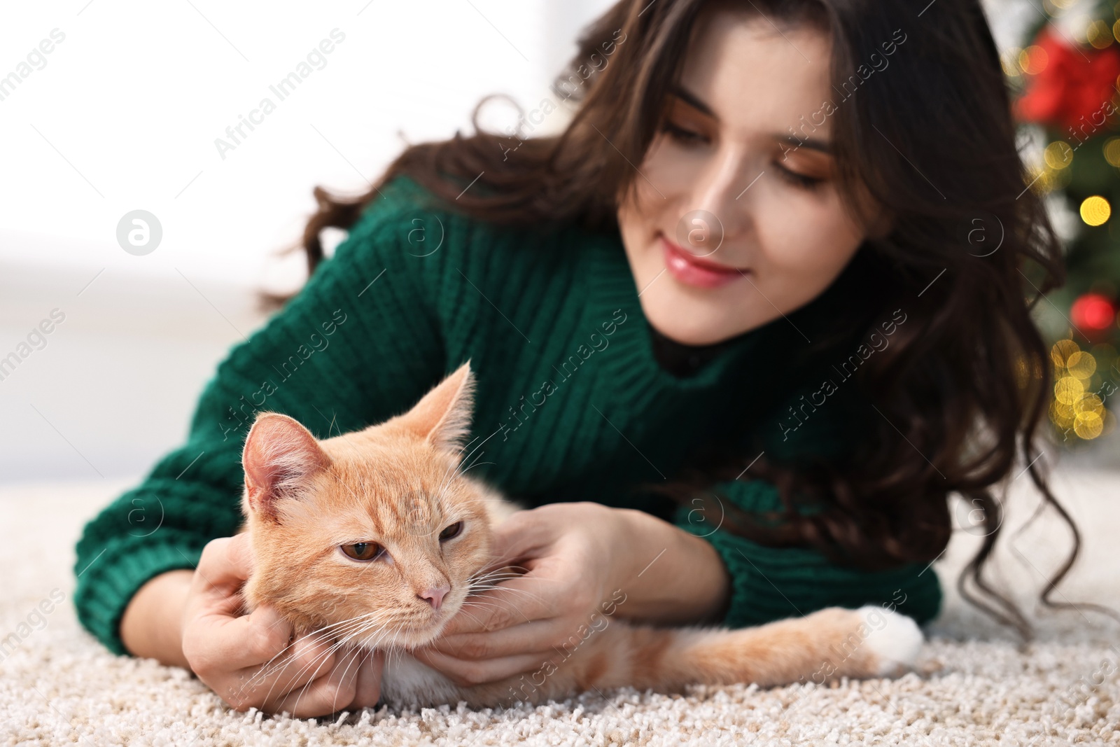 Photo of Woman with cute ginger cat lying on rug in room decorated for Christmas