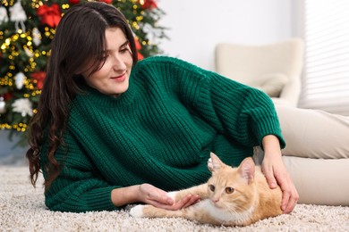 Woman with cute ginger cat lying on rug in room decorated for Christmas