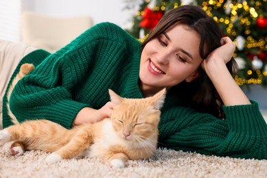 Woman with cute ginger cat lying on rug in room decorated for Christmas