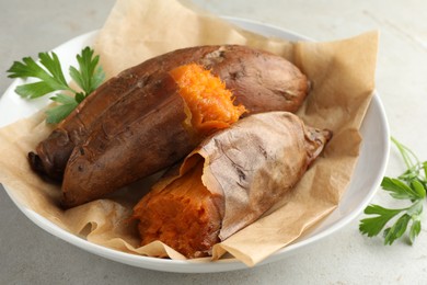 Photo of Tasty cooked sweet potatoes served with parsley on light grey table, closeup