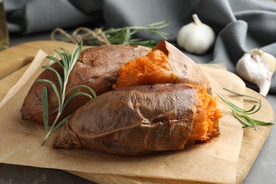 Photo of Tasty cooked sweet potatoes served with rosemary on grey table, closeup